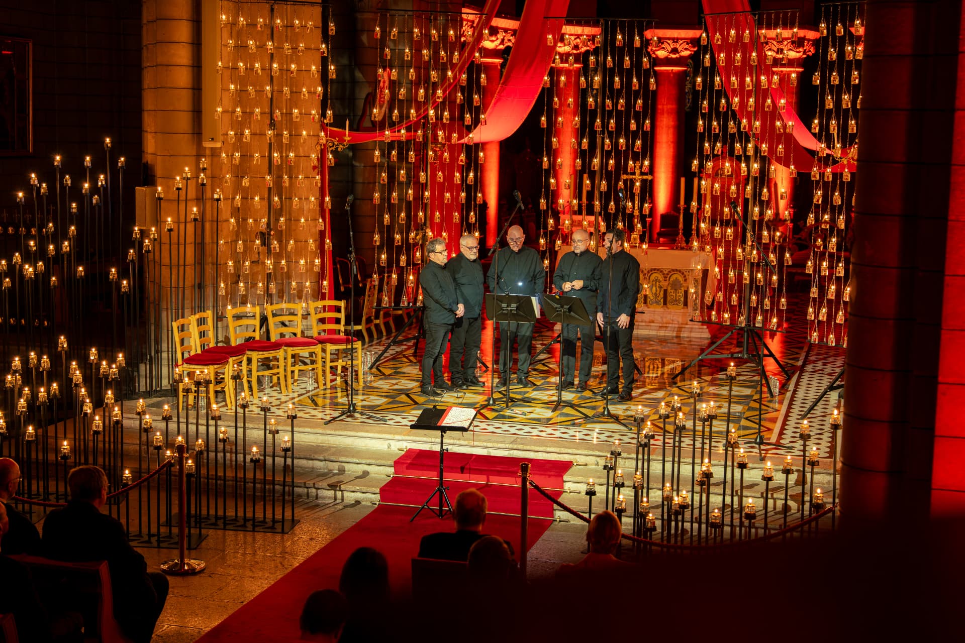 Un ensemble vocal masculin au milieu des bougies et de tentures rouges